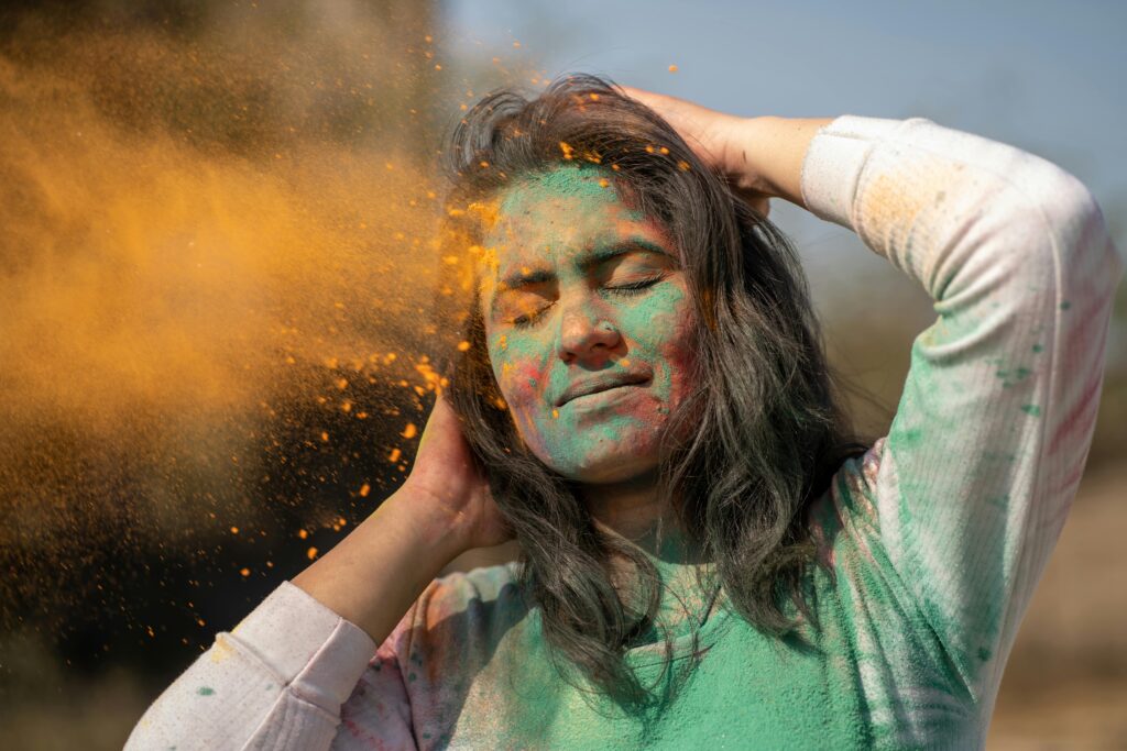 Young woman enjoying Holi festival with vibrant color powder on her face.